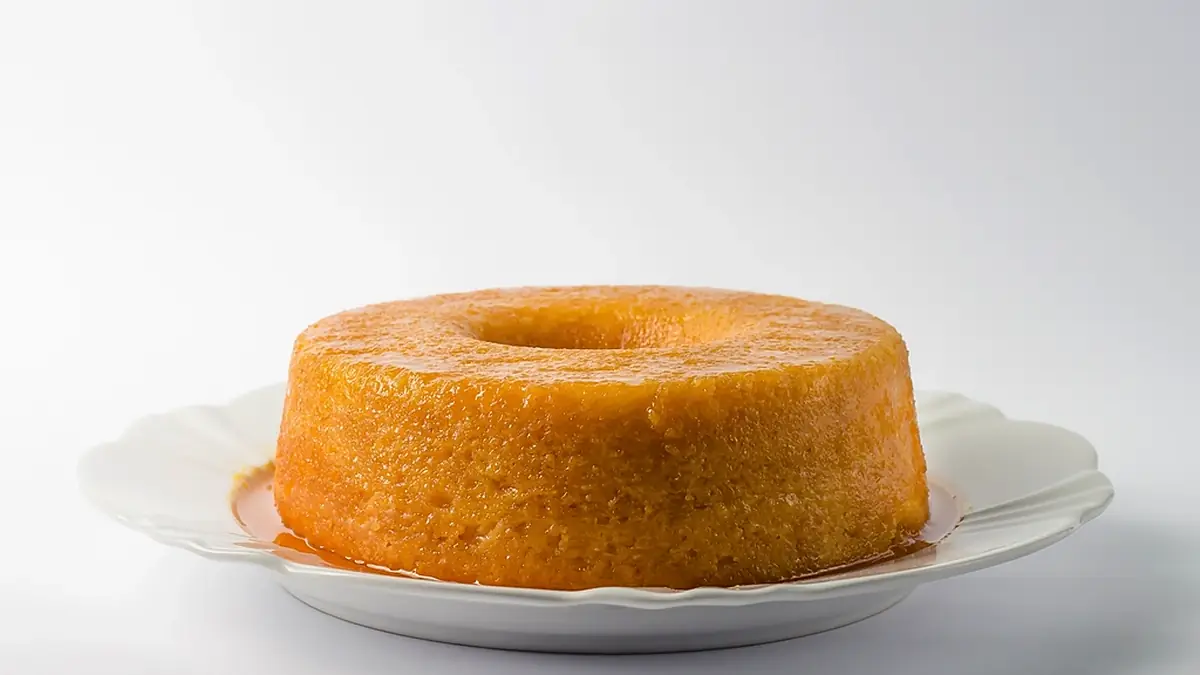 Bolo de laranja com furo no meio e calda, num prato branco