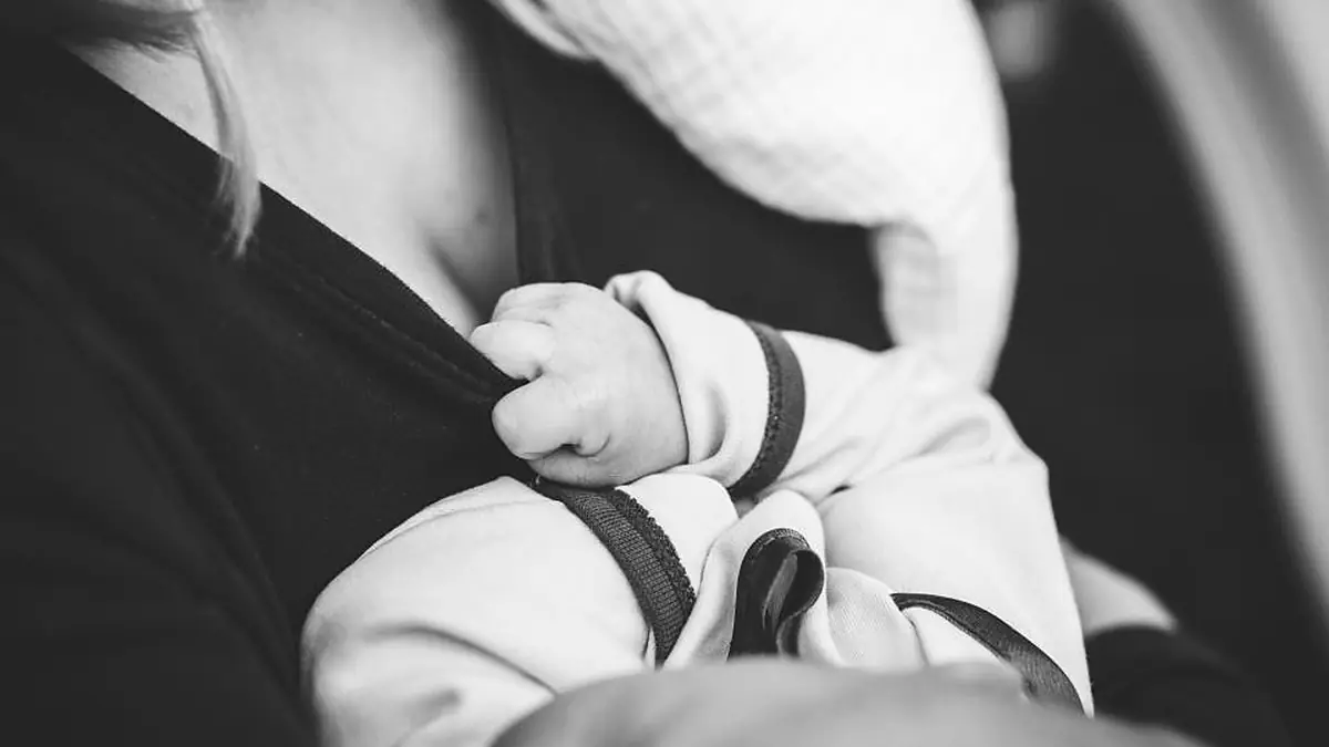 Mãozinha de bebê segurando a roupa da mãe, no colo, em preto e branco