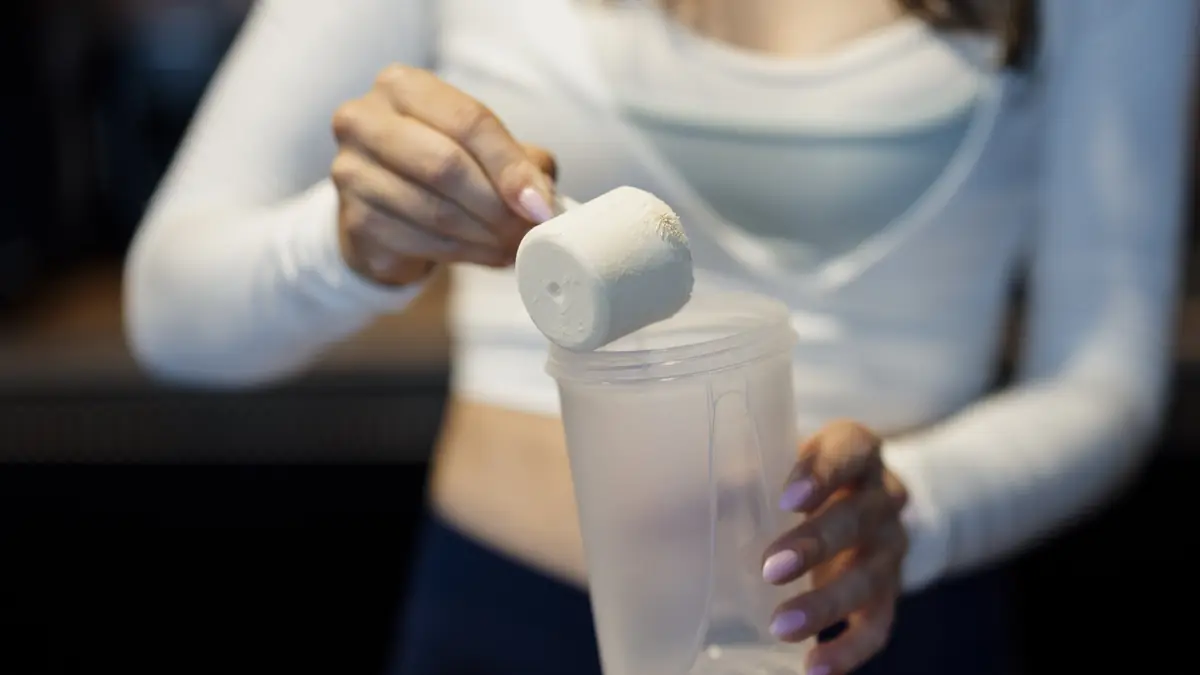 Pessoa colocando uma medida de proteína em pó numa coqueteleira